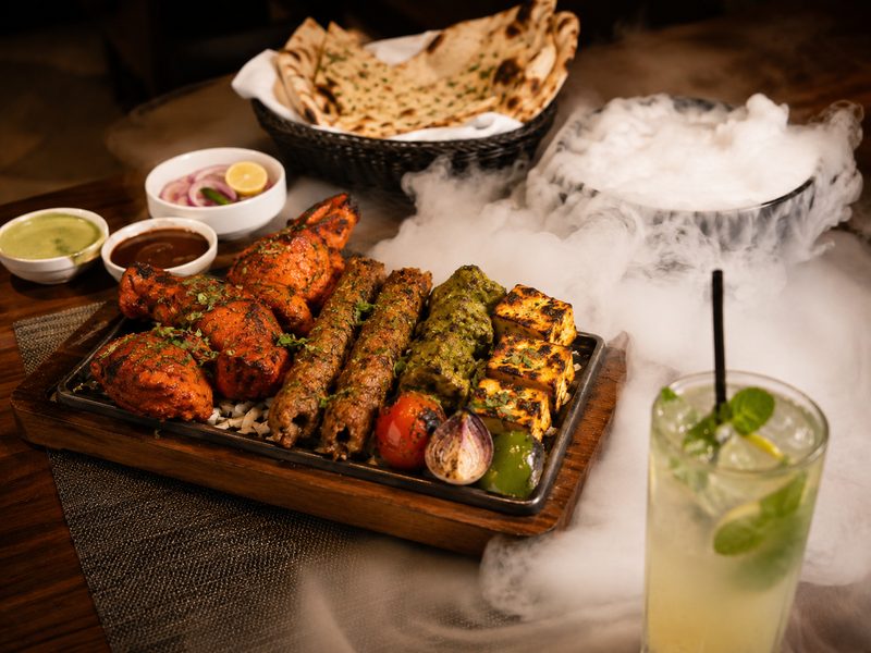 Tandoori platter served on a sizzler with a nitrogen-smoked drink alongside